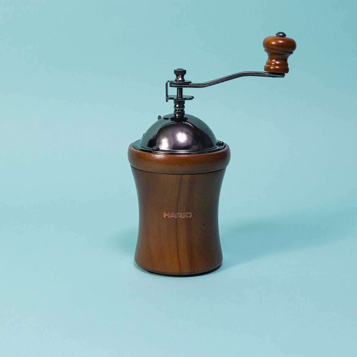 Round wooden grinder tapered in the middle with dark metal dome on top with wooden knobbed metal handle