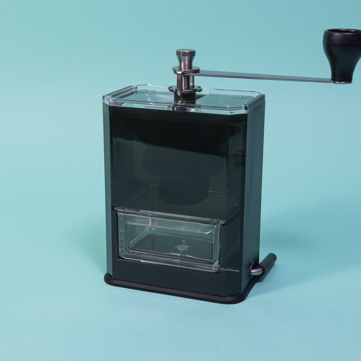 Dark black acrylic monolithic grinder body with clear drawer and  grinding handle on top, and smaller lever on bottom.