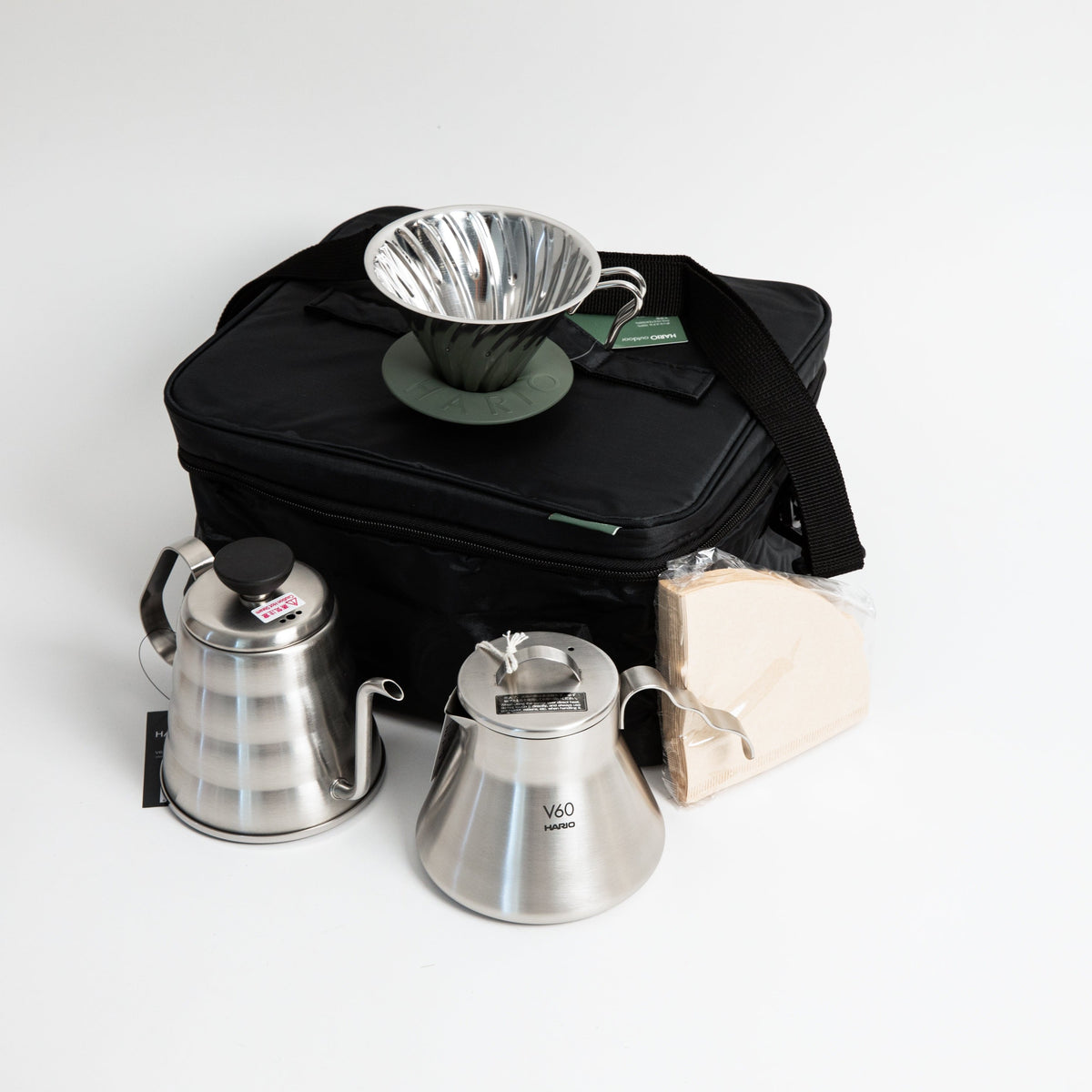 stainless steel kettle, metal cone coffee dripper with a olive green base stainless steel coffee sever pot, stainless steel lid and coffee filters with a black bag. on a white background.