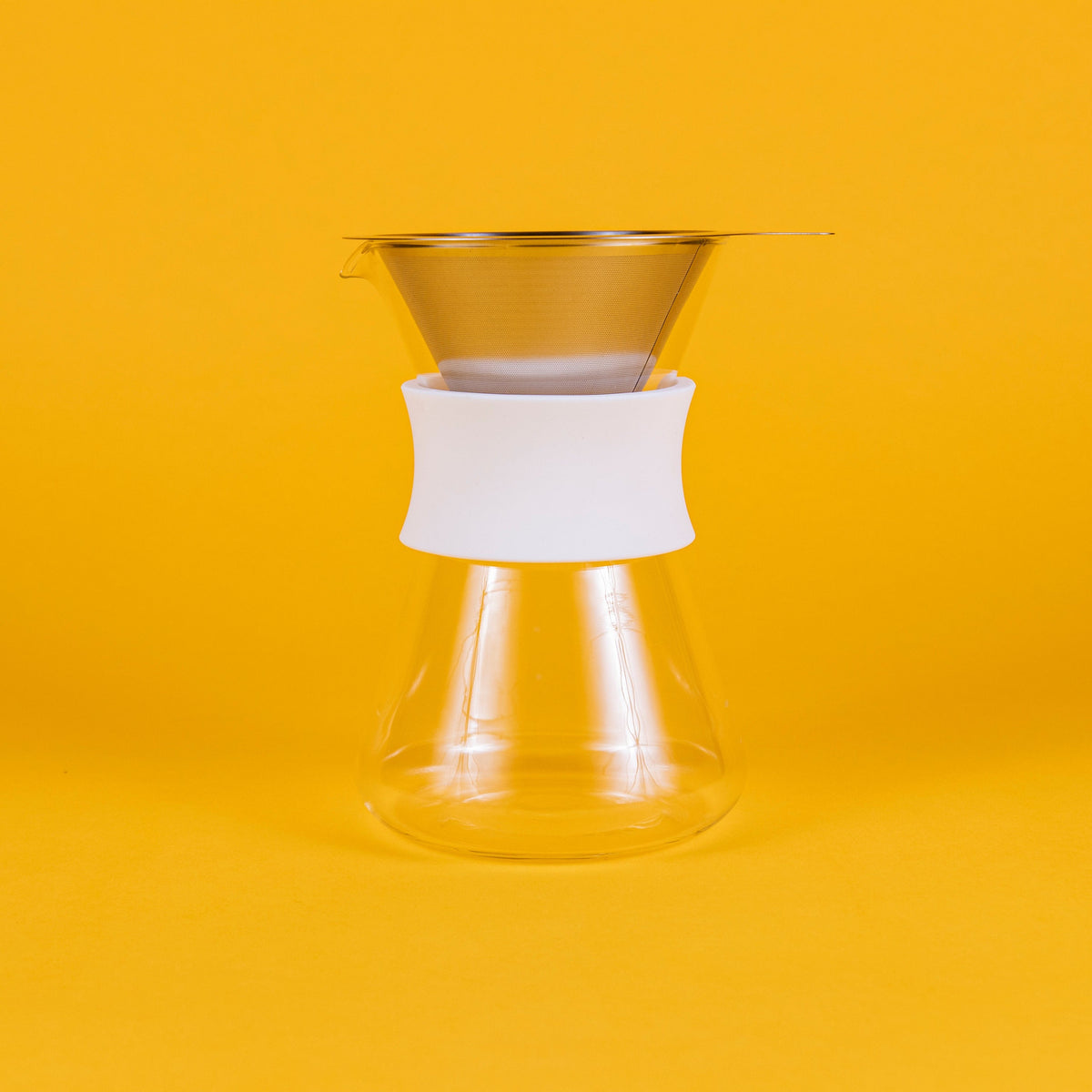 Clear glass server with white silicone collar and stainless steel mesh filter against a yellow background.