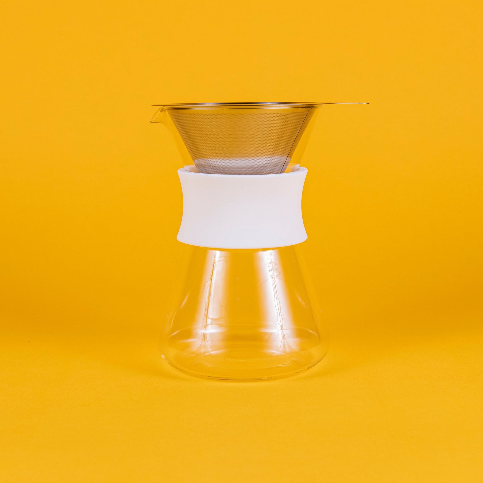 Clear glass server with white silicone collar and stainless steel mesh filter against a yellow background.