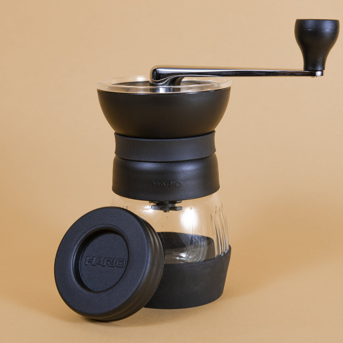 Black plastic coffee mill with handle attached to a glass container via screw top with a rubber base, and plastic lid.