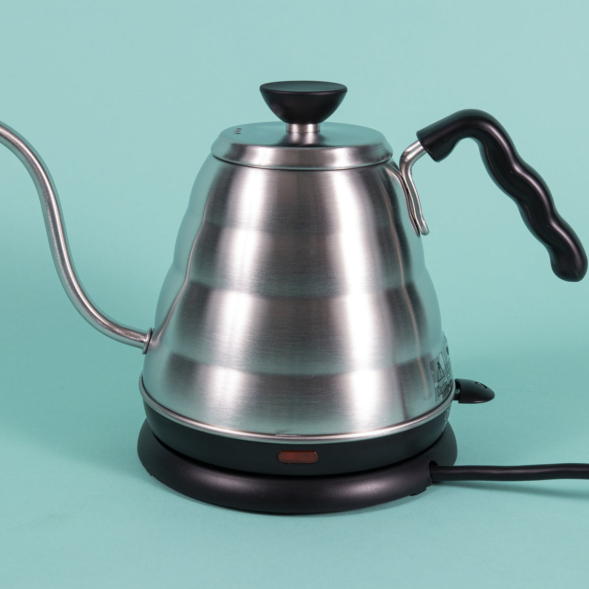 Stainless steel gooseneck kettle and matching lid with plastic base with red LED knob and black plastic covered handle on top a heating base with powercord on a teal backdrop.