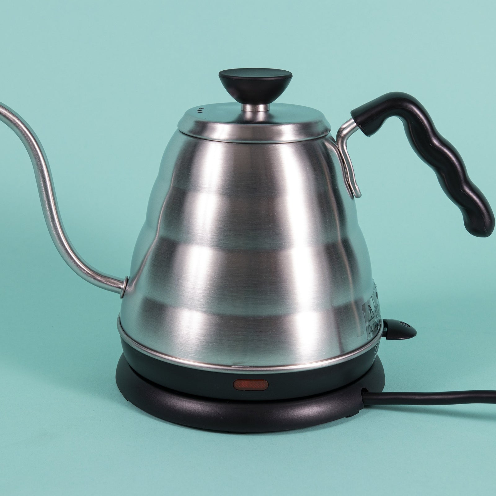 Stainless steel gooseneck kettle and matching lid with plastic base with red LED knob and black plastic covered handle on top a heating base with powercord on a teal backdrop.