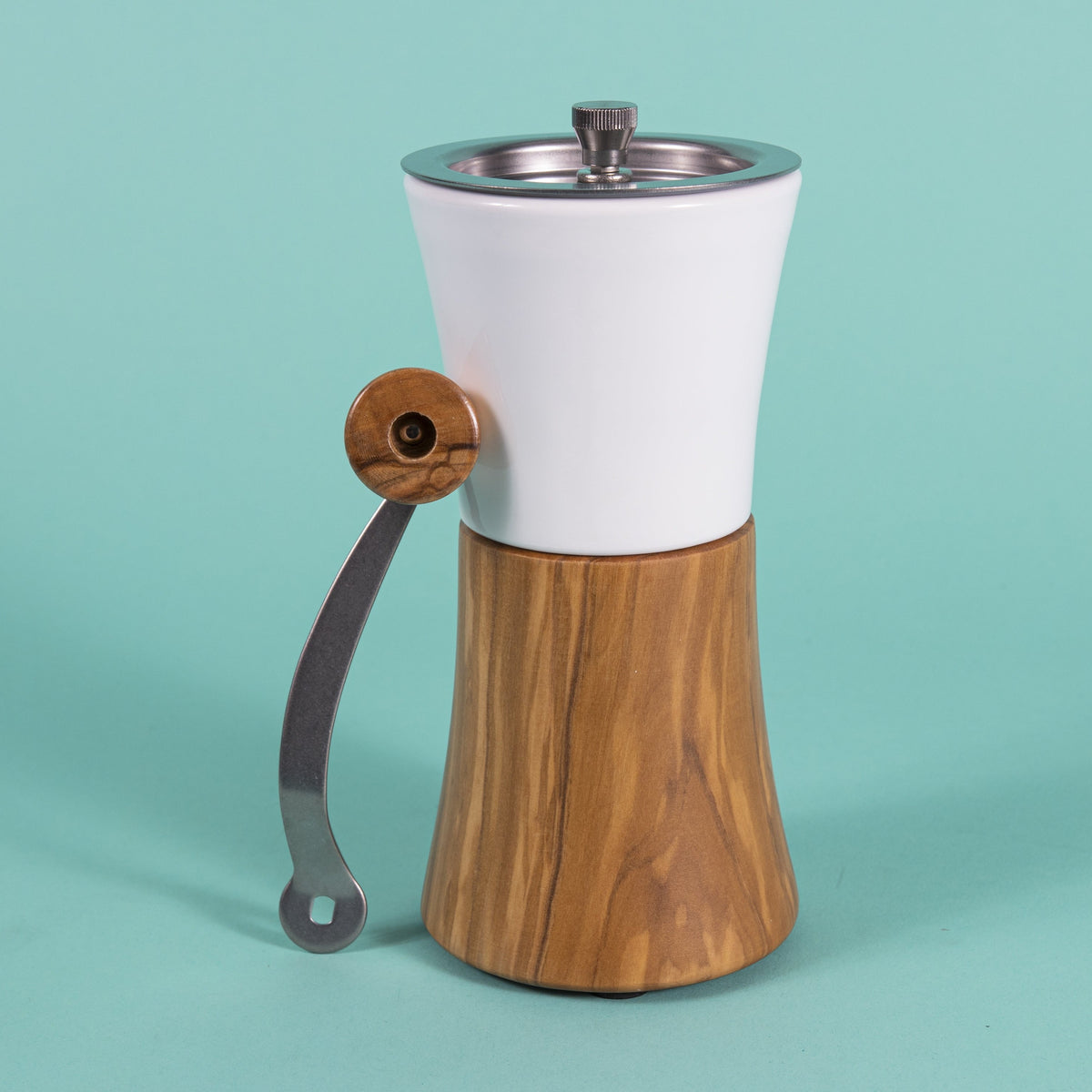 Hour glass shaped coffee hand grinder with olive wood base, white ceramic neck, stainless steel grinder assembly and screw, stainless steel handle with olive wood knob resting against grinder, and set against a blue background.