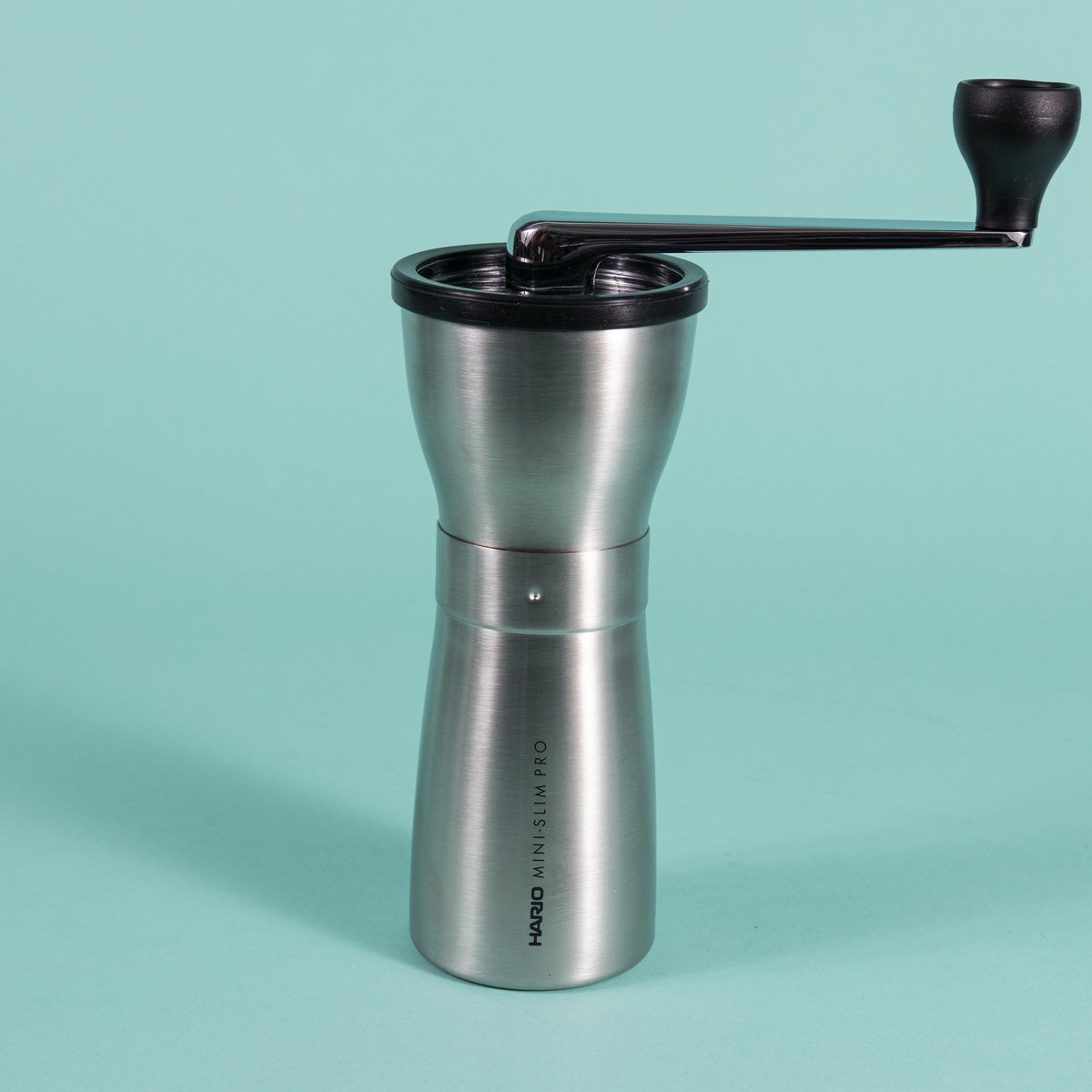 Slim silver metal coffee grinder with rubber lid and metal lever with black plastic knob at the end.