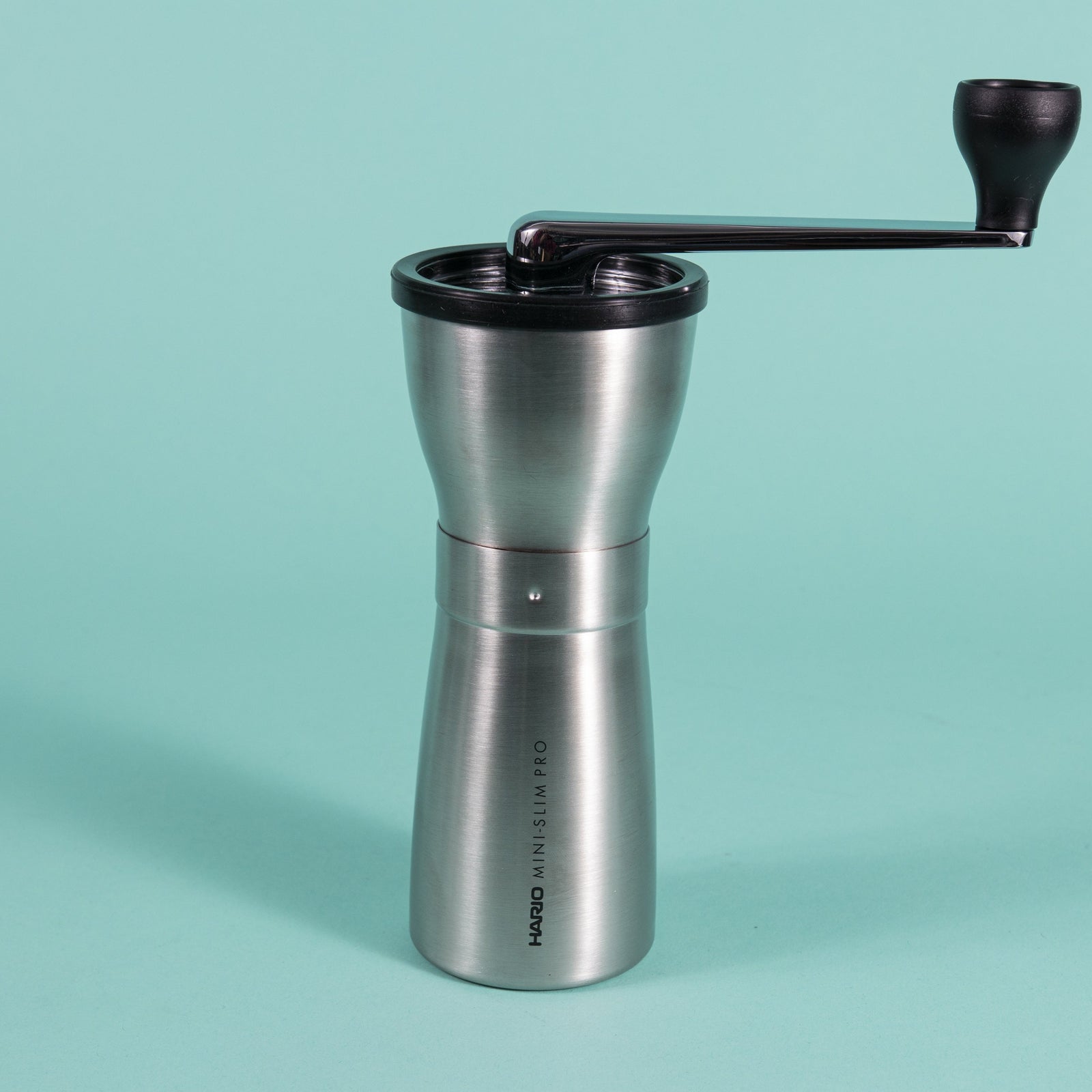 Slim silver metal coffee grinder with rubber lid and metal lever with black plastic knob at the end.