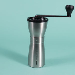 Slim silver metal coffee grinder with rubber lid and metal lever with black plastic knob at the end.